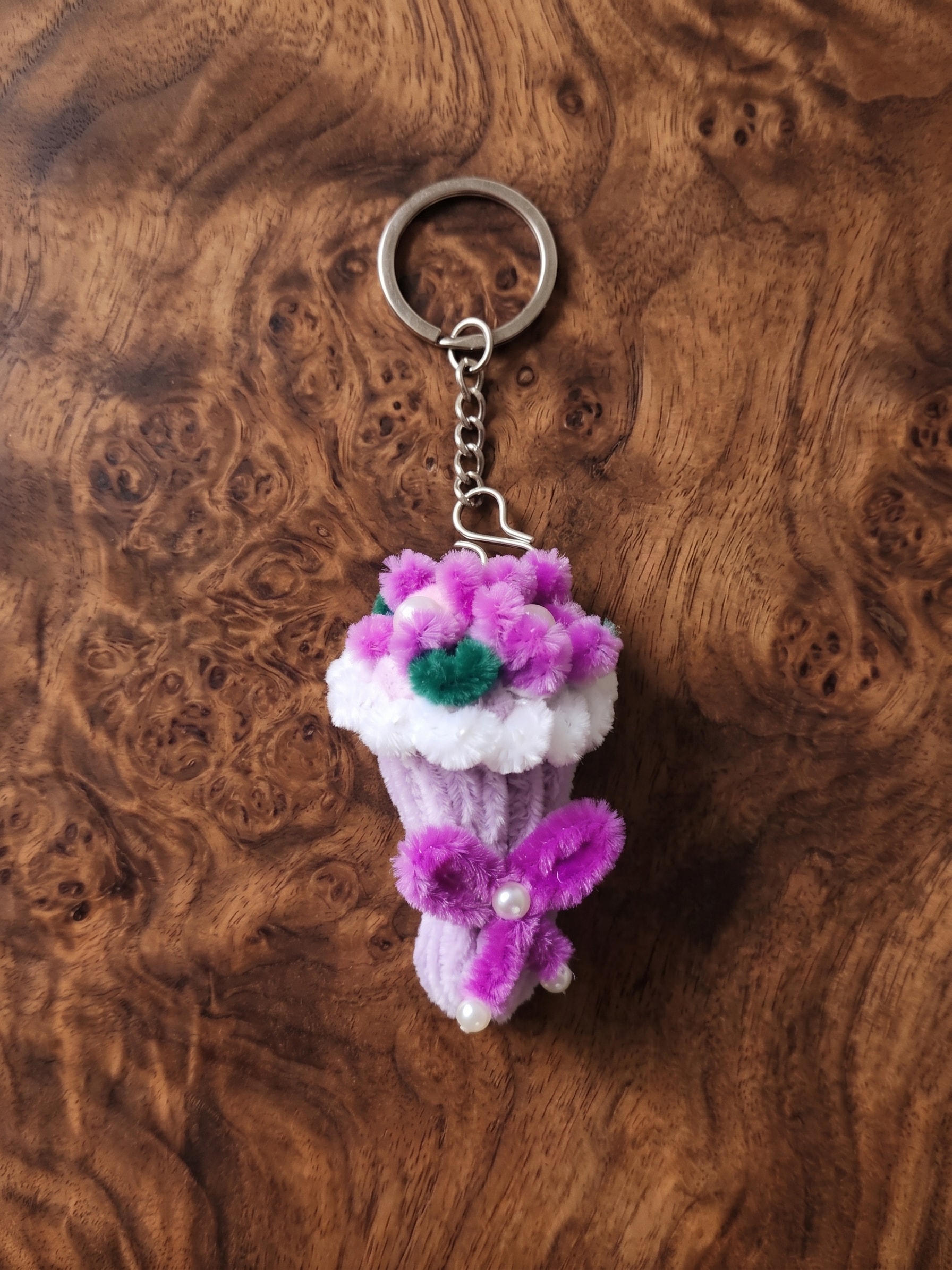 Bloom Cup Keychain โ A cute handmade floral keychain featuring a soft lavender cup-style charm, bright pink flowers, green leaf details, pearl-style accents, and a matching dangling flower. Perfect for handbags, backpacks, purses, and gifting.